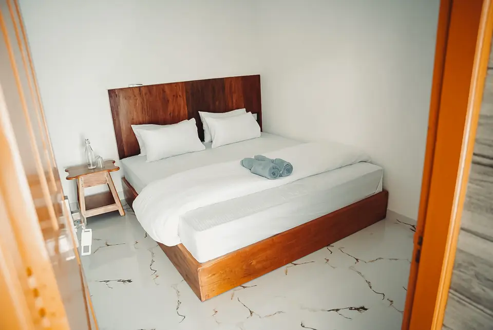 A double bed with white linen and a wooden headboard, seen through an open wooden door frame