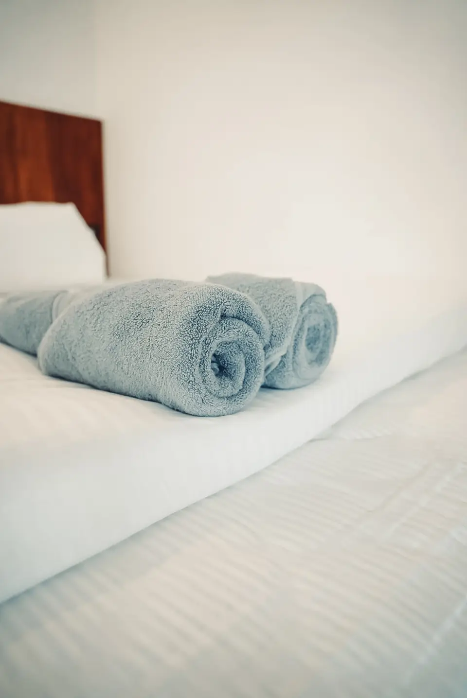 Rolled towels laid out on a freshly made bed