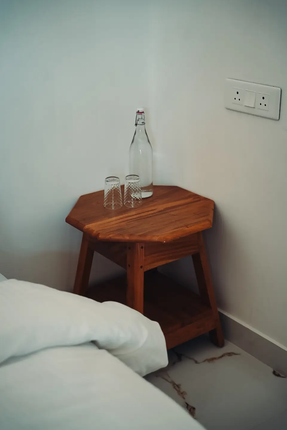 Close-up of white bedding folded over the edge of a bed, with wooden stool legs and a marble-effect floor behind