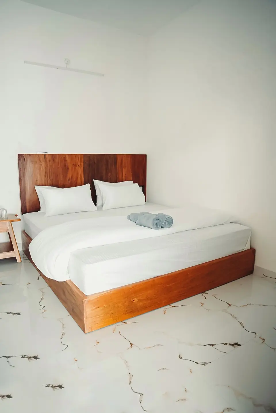 A made-up double room at Kuma Surf with a teak bed and white linen