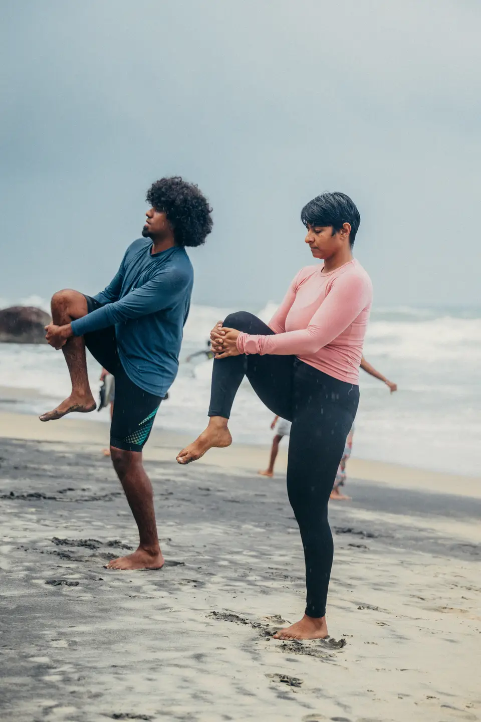 An instructor taking a student through a warm-up stretch on the sand