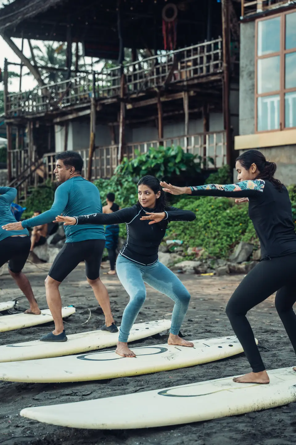 Four people hold pop-up stances on soft-tops laid in a row on the sand, a timber building with balconies behind