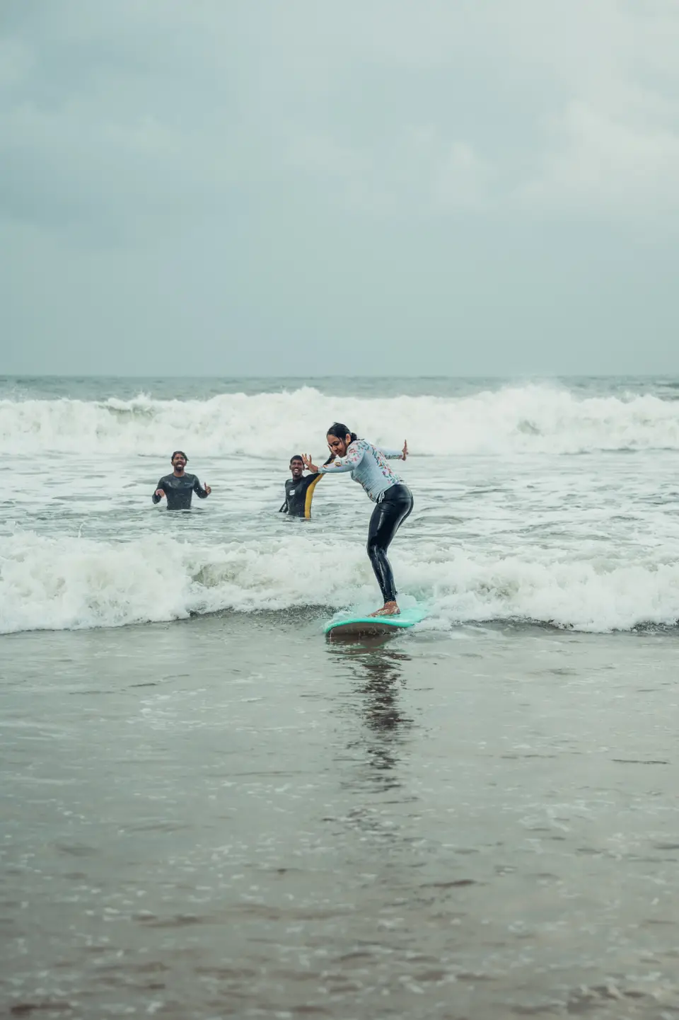 A first-time surfer standing up on a soft-top board in whitewater at Edava