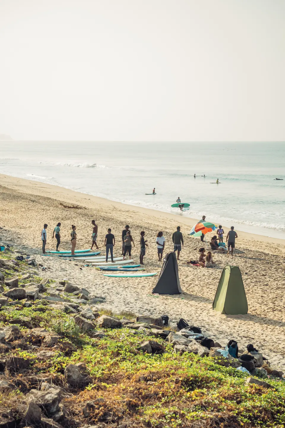 A surf group gathered in a circle on the sand, seen from above the beach